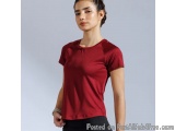 The image shows a young woman wearing a red t-shirt and black pants. She is standing in front of a plain grey background and...