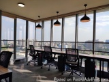 The image shows an empty office space with a large window that offers a panoramic view of the city. The room has a long woode...