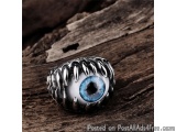 The image is a close-up of a ring with a blue eye in the center. The eye is surrounded by a silver band with a textured desig...