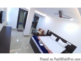 The image shows a modern and spacious bedroom with a large bed in the center. The bed has a black headboard and white linens...
