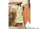 The image shows a young woman standing in front of a white wall with a wooden surfboard leaning against it. She is wearing a...