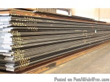 The image shows a stack of steel plates in a warehouse. The plates are arranged in a horizontal manner and are stacked on top...
