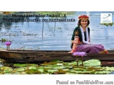 The image shows a woman sitting in a wooden boat on a lake. She is wearing a traditional Indian outfit with a red headscarf a...