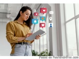 The image shows a young woman standing in an office or workspace, holding a tablet in her hands and looking at it intently. S...