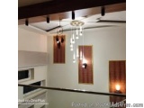The image shows a modern and elegant chandelier hanging from the ceiling in a room. The room has white walls and a wooden cei...