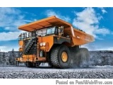 The image shows a large orange dump truck in a quarry. The truck is a large, articulated vehicle with a long, flatbed trailer...