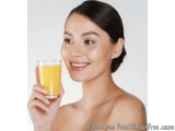 The image is a close-up portrait of a young woman holding a glass of orange juice. She is smiling and looking directly at the...