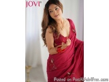 The image is a portrait of a young woman wearing a traditional Indian saree. She is standing in a room with a white curtain i...