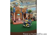 The image shows a colorful stage set up in a shopping mall. The stage is decorated with a blue and orange color scheme and ha...