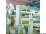 The image shows a large industrial machine in a factory. The machine is made of metal and has a yellow cylindrical shape. It...