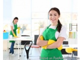 The image shows a young woman wearing a green apron and yellow rubber gloves, standing in a cleaning room with her arms cross...