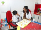 The image shows a young boy sitting at a red chair in a room with a woman sitting next to him. The boy is wearing a white shi...