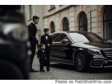 The image shows a black Mercedes-Benz car parked on a cobblestone street in front of a building with arched windows. There ar...