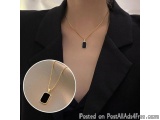 The image shows a close-up of a woman's neck and upper body. She is wearing a black blazer and a gold necklace with a pendant...