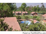 The image shows a group of red-roofed houses with a swimming pool in the center. The houses are surrounded by lush greenery a...