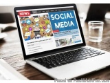 The image shows a laptop on a wooden table with a glass of water on the right side. The laptop screen displays the homepage o...