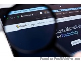 The image shows a magnifying glass hovering over a computer screen with the Microsoft Edge for Business website open. The web...