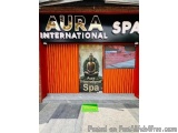 The image shows the entrance of Aura International Spa. The entrance is a red building with a black awning that reads "Aura I...