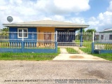 The image shows a small blue house with a white picket fence in front of it. The house has a sloping roof and a small porch w...
