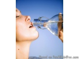The image shows a close-up of a woman's face and upper body. She is holding a clear glass bottle with a metal stopper in her...