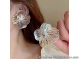 The image shows a close-up of a person's ear wearing a pair of earrings. The earrings are made of silver metal and have a flo...