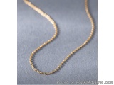The image shows a gold chain necklace lying on a gray background. The necklace is made up of small, round beads that are arra...