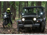 The image shows a black Jeep Wrangler parked in a wooded area. The Jeep has a license plate that reads "UK 04Z5557". A person...