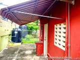 The image shows a red building with a white door and a window on the right side. The building appears to be a small, single-s...