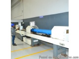The image shows a large industrial machine in a factory. The machine is white in color and has a long, rectangular shape with...