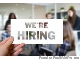 The image shows a hand holding a white card with the words "WE'RE HIRING" written in bold black letters. The background is bl...