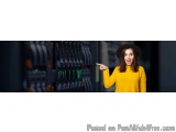 The image shows a young woman wearing a black hat and a yellow sweater. She is standing in front of a rack of servers and is...
