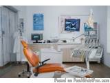 The image shows a modern dental clinic with an orange dental chair in the center. The chair has a high backrest and armrests,...