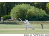 The image shows a cricket match in progress. The batsman is in the middle of his swing, with his bat extended and his body sl...