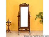 The image shows a wooden floor-standing mirror with a tall, ornate frame. The frame is made of dark wood and has a carved des...