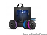 The image shows a 3D printer with three spools of filament in front of it. The printer is black in color and has a handle on...