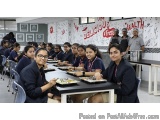 The image shows a group of young girls sitting at a long table in a cafeteria. They are all wearing school uniforms and are s...