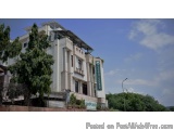 The image shows a modern building with a white exterior and a green roof. The building appears to be a hotel or a residential...