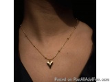 The image shows a close-up of a person's neck and upper chest area. The person is wearing a gold necklace with a small heart...