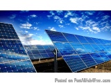 The image shows a large array of solar panels in a field. The panels are arranged in a grid-like pattern and are evenly space...