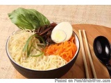 The image shows a bowl of ramen noodles with a variety of ingredients. The bowl is black and is placed on a wooden cutting bo...