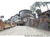 The image shows a modern building with a curved glass facade. The building is located on a hillside with trees and bushes sur...