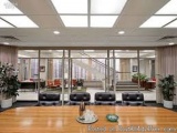 The image shows a modern office space with a large wooden table in the center. The table is surrounded by six black leather c...