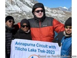 The image shows a group of five people standing together and holding a banner that reads "Annapurna Circuit with Tilicho Lake...