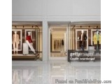 The image shows the entrance of a clothing store. The store has three large glass windows with mannequins wearing different o...