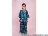 The image shows a young girl standing against a pink background. She is wearing a blue top with white floral patterns on it a...