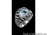 The image is of a silver ring with a large blue eye in the center. The eye is surrounded by a textured design that resembles...