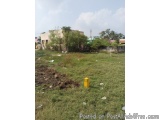 The image shows an empty field with a yellow post box in the center. The field is covered in grass and there are a few trees...