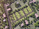 The image is an aerial view of a residential area. The area is surrounded by trees and there are several buildings scattered...