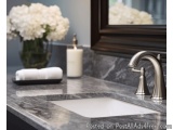 The image shows a modern bathroom sink with a marble countertop. The sink is white and has a silver faucet with a curved spou...