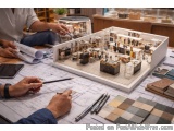 The image shows a group of people working on a model of a building. The model is placed on a table with various architectural...